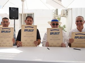 ארבעה מנהלים יושבים על שולחן ומחזיקים בידם קלף הנחת אבן פינה למרלוג דיפלומט